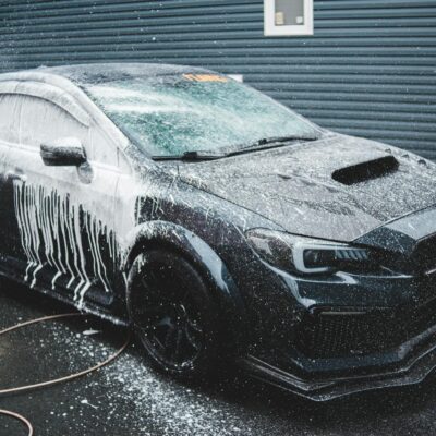 Black expensive tuned sports car under car wash next to cottage in daytime