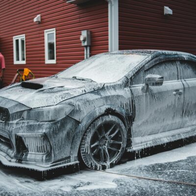 Unrecognizable African American worker standing by luxury sports car covered with foam at car wash in daytime