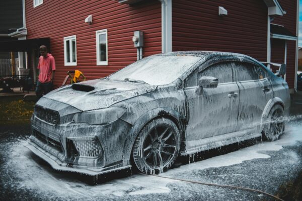 Unrecognizable African American worker standing by luxury sports car covered with foam at car wash in daytime